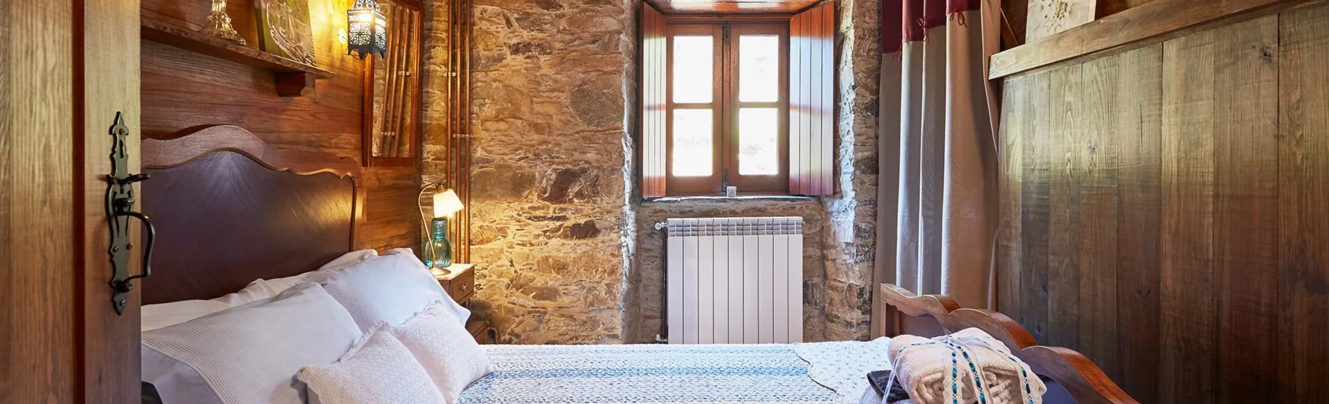Bedroom with a double bed and a solid wood headboard against a schist wall